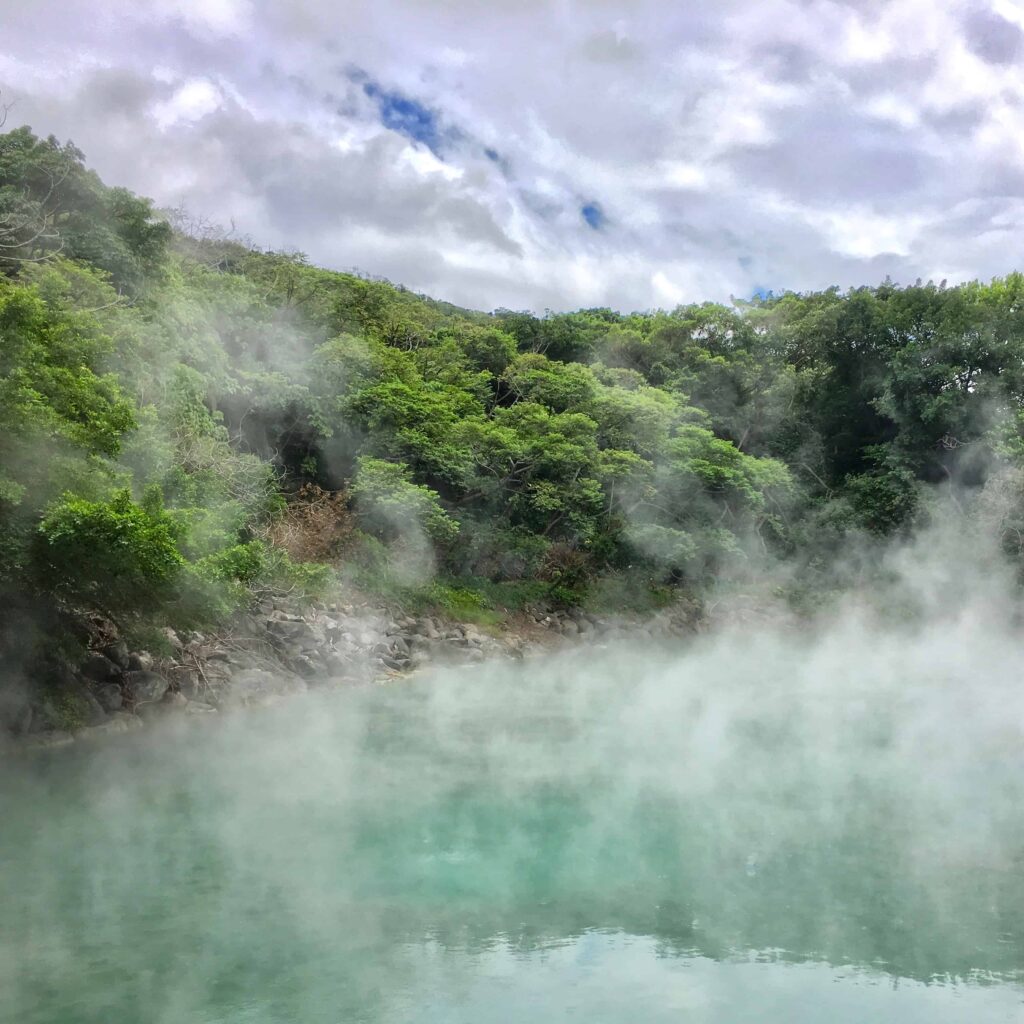 Beitou Hell Valley. Steaming hot spring with green mountain backdrop and fluffy white clouds in blue sky